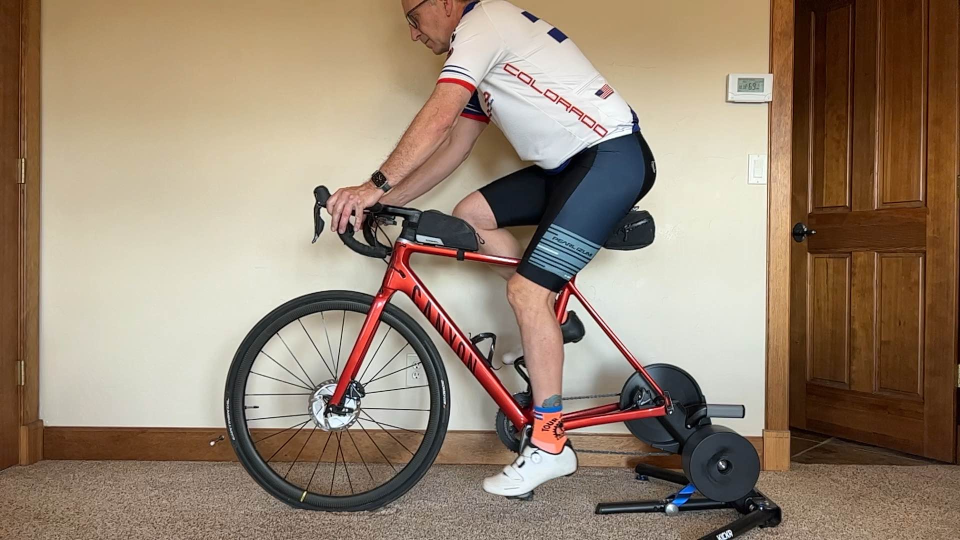 A rider on an indoor trainer, side view, set up correctly for recording: even front lighting, plain wall behind, close-fitting clothing.
